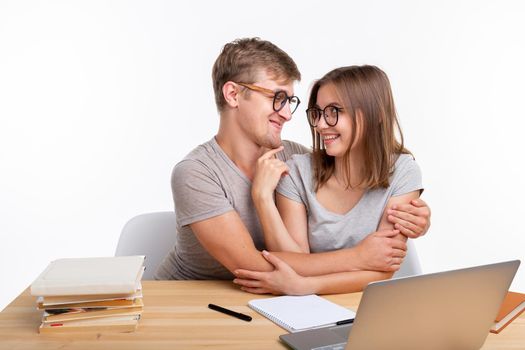 People and education concept - Two fallen in love funny students sitting at the wooden table with laptop and books.