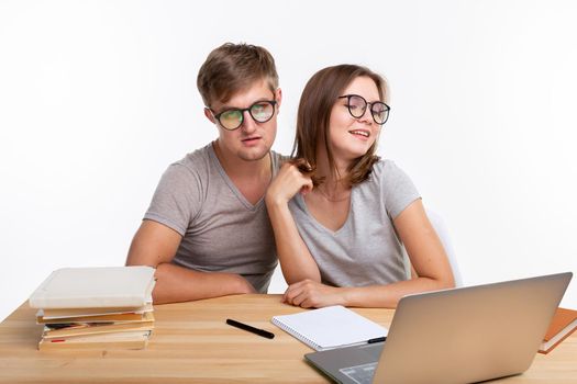 People and education concept - Two fallen in love funny students sitting at the wooden table with laptop and books.