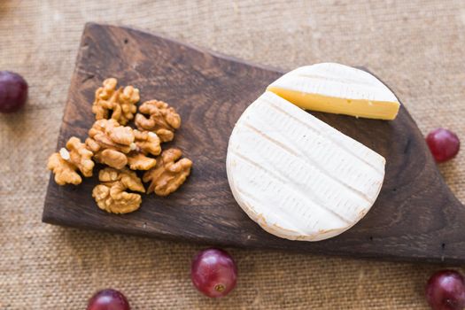 Brie or camembert cheese with nuts and grapes on a wooden board.