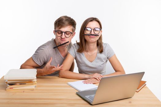 Education and people concept - a couple of young students in glasses look like they are bored of learning homework and make a stupid jokes.