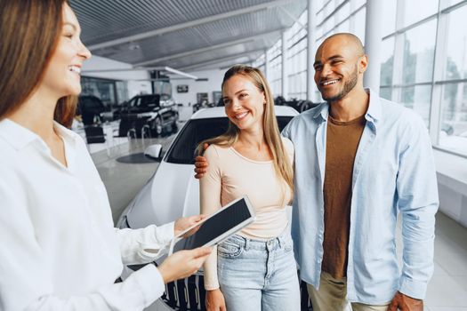 Car saleswoman in a car dealership having a talk with clients buyers