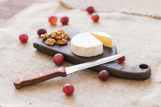 Brie or camembert cheese with nuts and grapes on a wooden board.