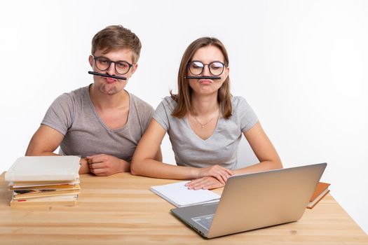 Education and people concept - a couple of young students in glasses look like they are bored of learning homework and make a stupid jokes.