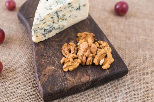 Slice of Blue cheese with nuts and grapes on a rustic background.