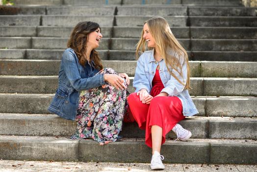 Two young women talking and laughing on urban steps. Two girls wearing casual clothes. Lifestyle concept.