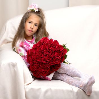 Happy little girl with a bouquet of flowers sitting on the couch. The concept of a holiday, spring mood, birthday and family happiness.