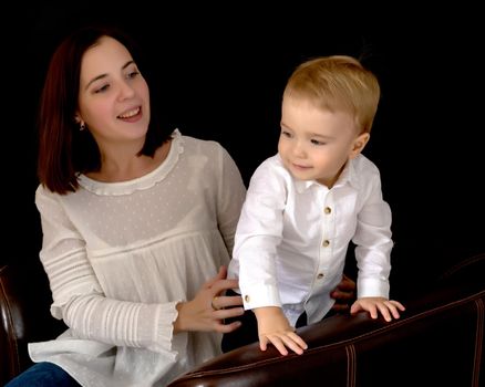 Young mother with a small son in her arms on a black background. The concept of a happy childhood, advertising.