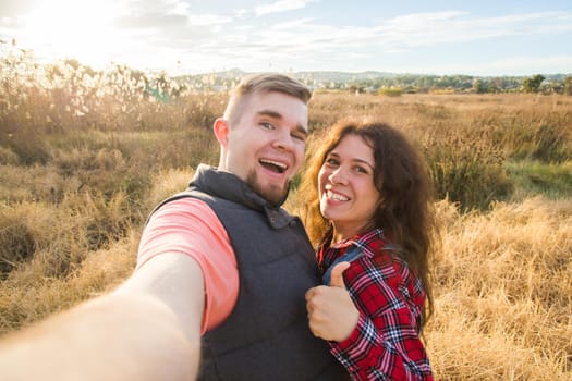 Travel, tourism and nature concept - Smiling couple taking selfie on field and showing thumbs up.