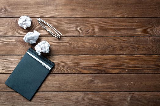 Top view of well organized home office workplace. Black spiral notepad, crumpled paper and glasses on brown wooden surface. Education, creativity and working minimalist concept with copy space.