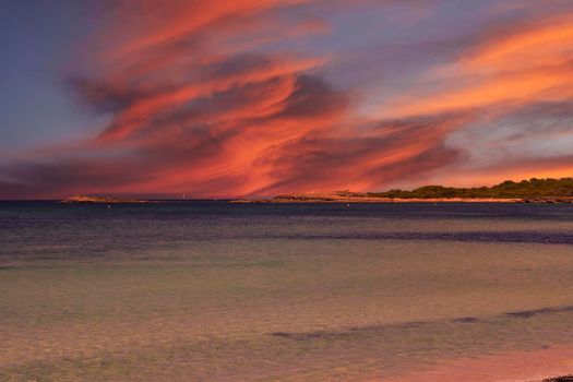 Transparent bay on a sunny day with orange-coloured clouds. Turquoise water. Vegetation, Balearic Islands. Mediterranean Sea