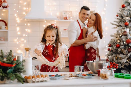 A little girl in the New Year's kitchen makes dough, and her mom and dad are watching next to her.