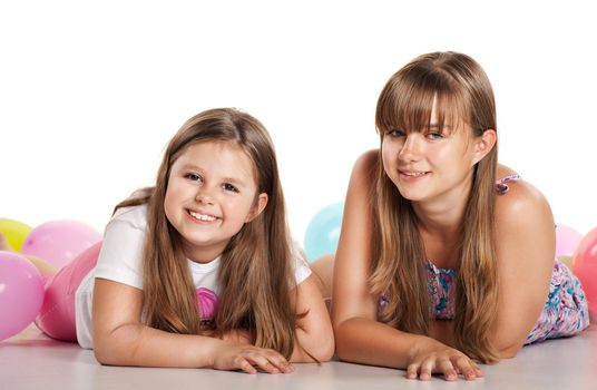 Two sisters lying on the floor with balloons on white background