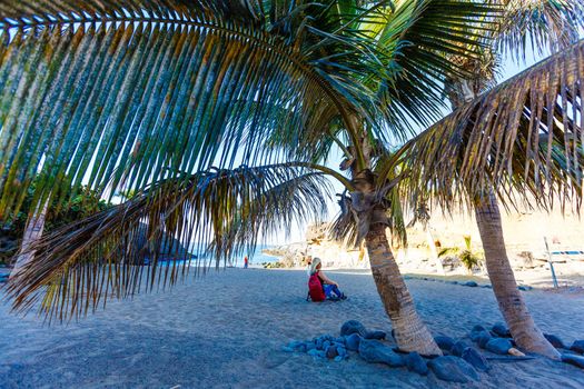 Freelancer girl on vacation by the sea under palm tree. Alone with yourself concept. Blogger dreamily looks at the sea