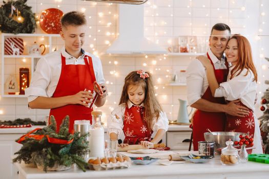 A little girl in the New Year's kitchen makes dough and her family helps her.