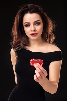 Smiling girl holding a gambling chips in her hands on black background. Sexy brunette in a dress. Poker.