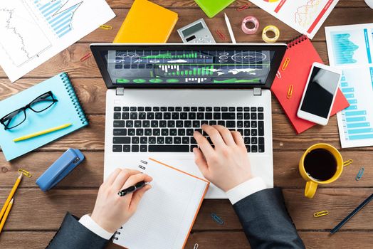 Close up business analyst working at laptop. Top view office workplace with computer and financial documents. Business occupation design with man in business suit sitting at vintage wooden desk.