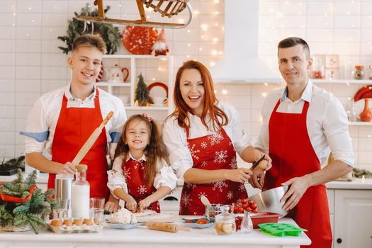 A happy family is standing in the Christmas kitchen and preparing dough for making cookies.