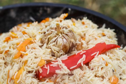 Cooking pilaf rice in a large cast iron pot over the fire. Garlic bulb and red hot pepper