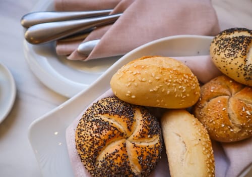 Fresh bread on a white plate with a napkin. Table setting in a restaurant