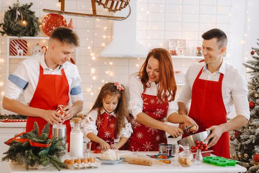 A happy family is standing in the Christmas kitchen and preparing dough for making cookies.