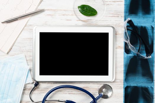 Mock up of doctors desktop with medical supplies. Tablet computer, x-ray image, stethoscope and cardiogram lies on wooden desk. Professional healthcare technology. Medical consultation and treatment.