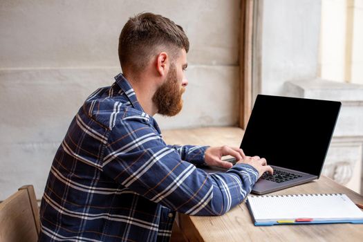 Young man chatting via net-book during work break in coffee shop, male sitting in front open laptop computer with blank copy space screen for your text message or advertising content