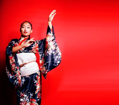 young pretty geisha on red background posing in kimono, oriental