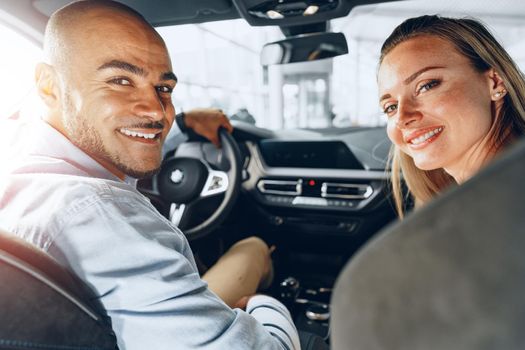 Joyful young couple looking around inside a new car they are going to buy in a car shop dealership