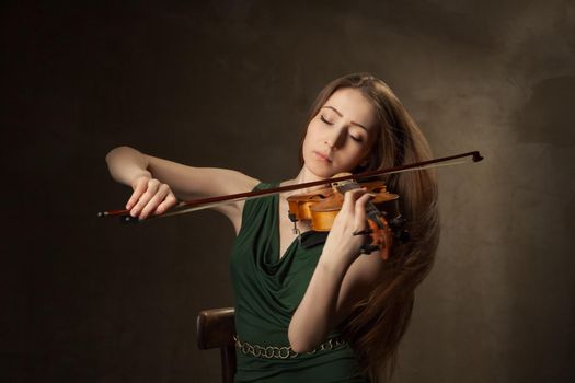 Beautiful young woman playing violin over black background