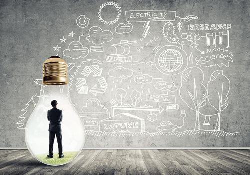 Businessman inside of light bulb in empty concrete room and sketches on wall