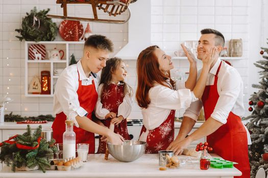 A happy family is standing in the Christmas kitchen and smearing each other with flour.