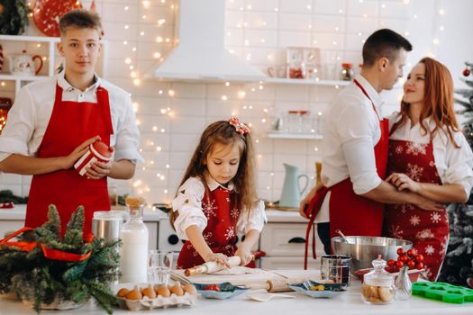 A little girl in the New Year's kitchen makes dough and her family helps her.