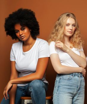 young pretty african and caucasian women posing cheerful together on brown background, lifestyle diverse nationality people concept close up