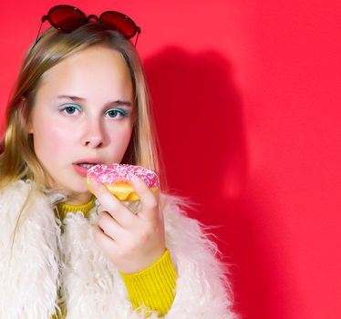 little cute blond teenage girl posing in fashion style with donut on red background, lifestyle people concept close up