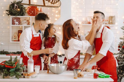A happy family is standing in the Christmas kitchen and smearing each other with flour.