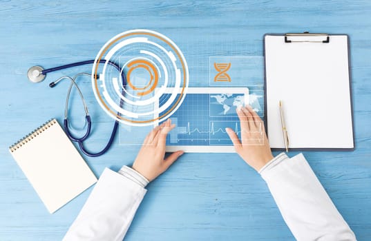 Top view of doctor hands with tablet computer. Therapist in white coat sitting at blue wooden desk. Examination and consultation in clinic. Medical application and online healthcare services.