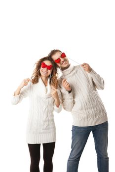 Portrait of joyful couple holding red hearts by their eyes and laughing