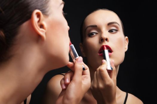 Beautiful sexy young woman hold lipstick near a mirror over black background