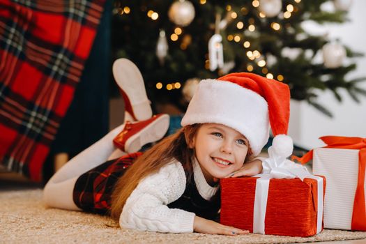 A happy little girl in a Santa Claus hat smiles with gifts in her hands.