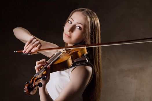 Beautiful young woman playing violin over black background