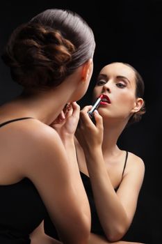 Beautiful sexy young woman hold lipstick near a mirror over black background