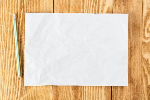 Business workspace with sheet of paper and pencil lying on wood table. View from above with copy space. Rectangular blank white paper on textured natural wooden background. Business presentation