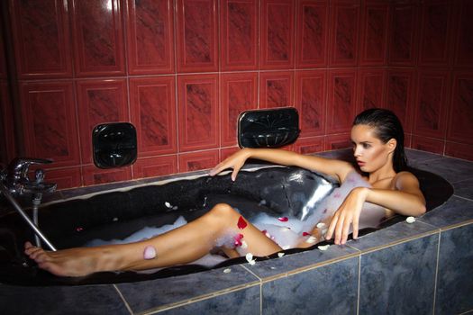 Beautiful woman relaxing in a black bathtub in red bathroom