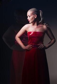 Young beautiful female model in red dress on black background