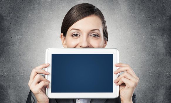 Businesswoman holding tablet computer with blank screen. Beautiful woman in business suit show tablet PC near her face. Corporate businessperson on grey wall background. Digital technology layout.