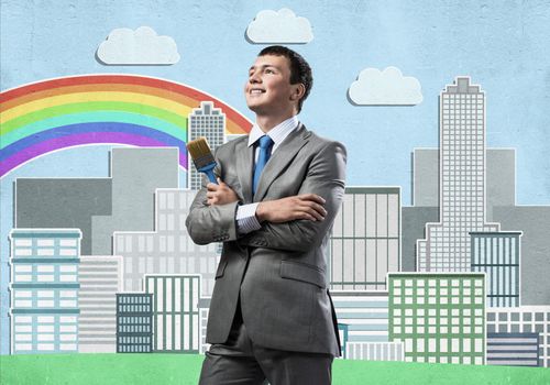 Confident and creative businessman painter standing with arms folded. Happy handsome man in business suit and tie holding paintbrush on city background. Cityscape illustration with colorful rainbow.