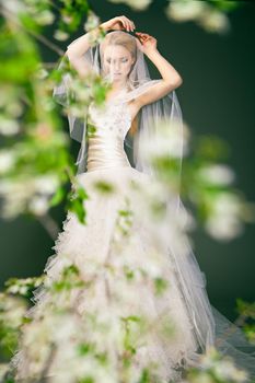 Portrait of a woman in wedding dress behind the green branches with flowers