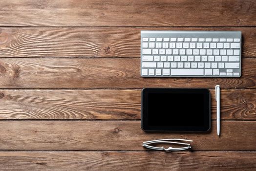 Top view of office workspace with gadgets. Flat lay hardwood plank desk with keyboard and tablet computer. Online accounting and banking. Digital technology in business. Vintage brown wooden surface