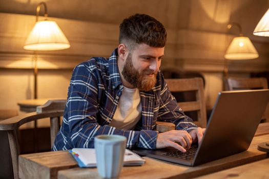 Young professional surfing the Internet on his laptop with cup of coffee on table at coffee shop or home office, working from cafe concept