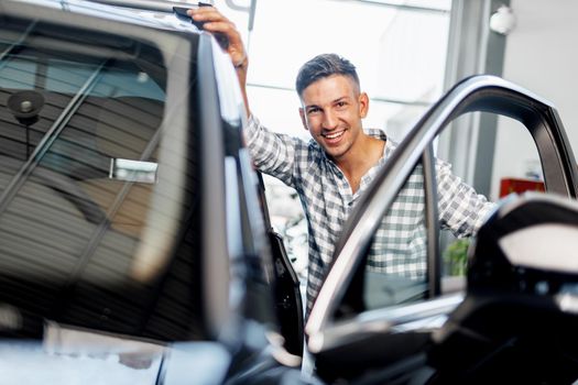 Cheerful young man customer buys a new car in a car dealership